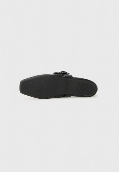 Sandal noir avec deux larges sangles dotées de boucles réglables, dessus en cuir lisse, semelle en caoutchouc texturé et design plat.