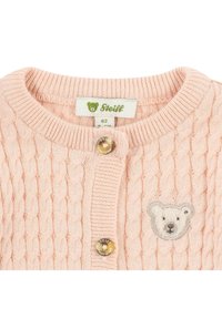 Svetle růžový pletený kardigan s kabelovým vzorem, zdobený výšivkou medvídka a kulatým zapínáním na knoflík. Na štítku je logo "Steiff".