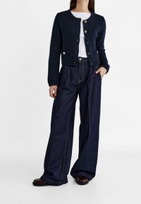 Navy knitted cardigan with round neckline and gold buttons, paired with wide-leg dark denim jeans featuring visible stitching and pockets.