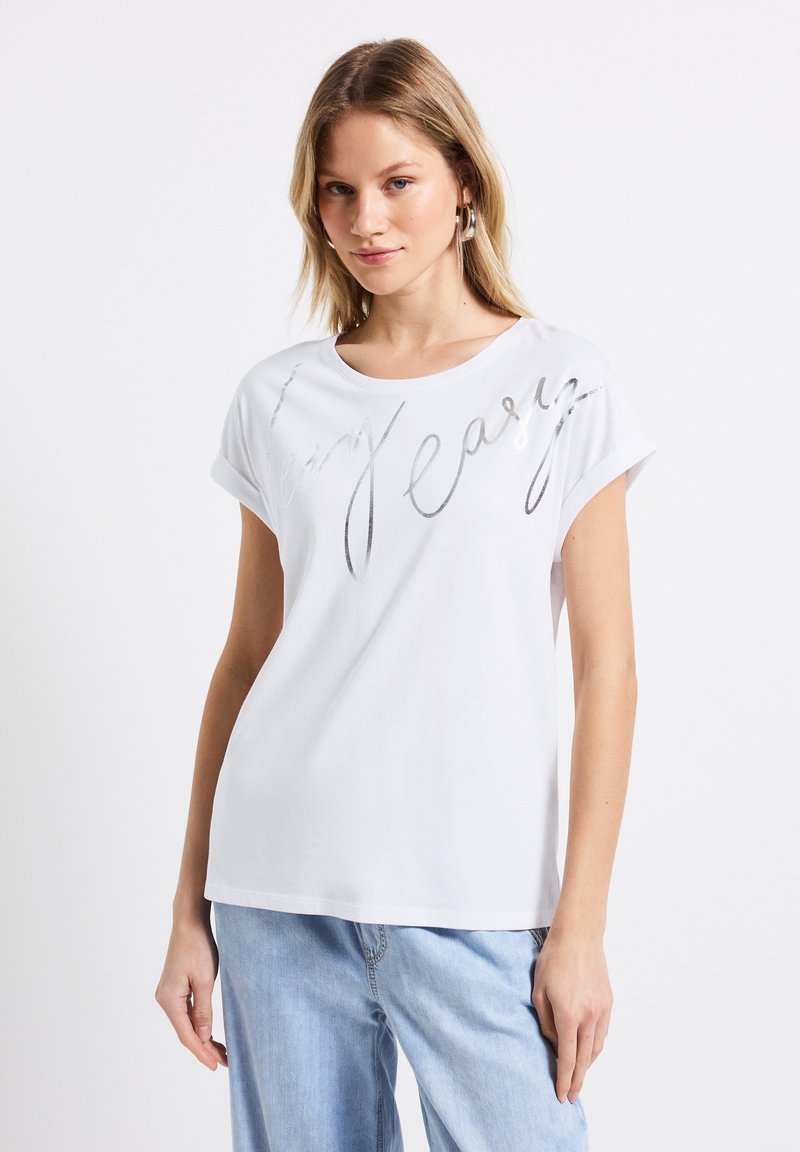 Camiseta blanca de manga corta hecha de material suave, con un estampado en script metálico plateado que dice "muy fácil" en la parte frontal. Corte casual.