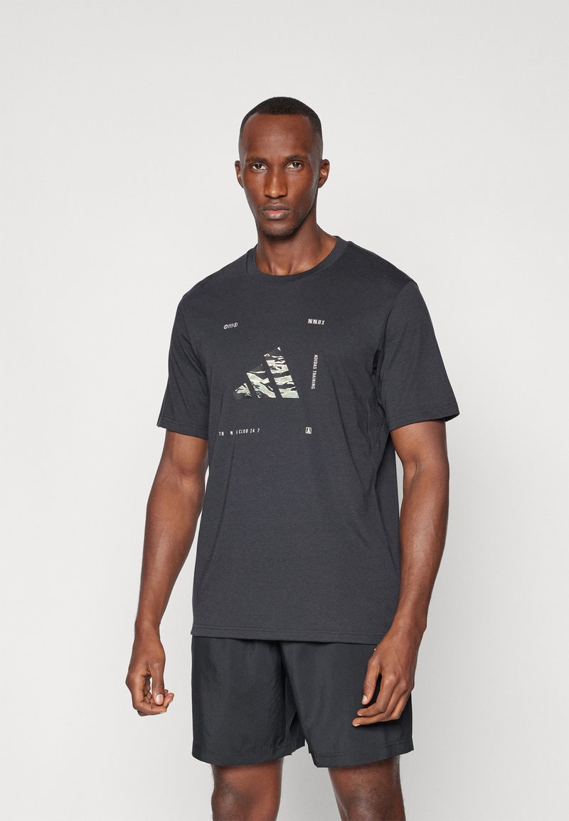 Camiseta negra de manga corta con un diseño gráfico que incluye un patrón de camuflaje y texto, fabricada en algodón, con un corte relajado.