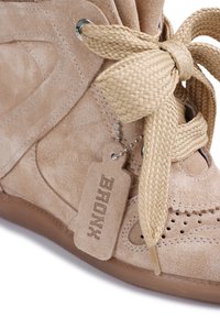 Baskets en daim beige avec de larges lacets tissés attachés en nœud, bouts perforés et une étiquette en daim portant l'inscription "BERONX" sur une chaîne à billes en métal.