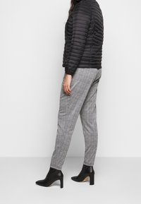 Giacca imbottita nera dal design leggero e trapuntato, abbinata a pantaloni su misura grigi e neri a quadri e stivaletti neri con tacco alto.