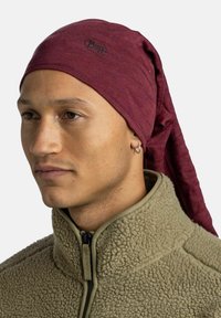 Maroon breathable headband made of stretchy fabric, featuring a logo, worn with a beige fleece jacket, showcasing a textured finish.