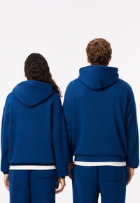 Felpe con cappuccio blu dal taglio morbido, con polsini a coste e tasca frontale. Entrambi sono abbinati a pantaloni blu coordinati.