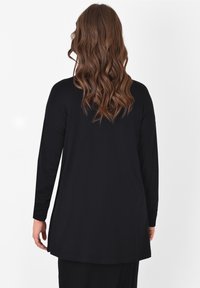 Svart långärmad topp med avslappnad passform, rund halsringning och en rundad fåll. Materialet verkar mjukt med en slät yta.