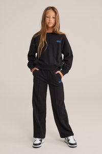 Hanorac negru și pantaloni asortați dintr-un material moale, cu accente de text albastru. Stilizați cu buzunare laterale și design cu picioare latisime.