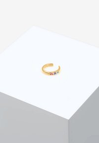 Anillo ajustable de color dorado que presenta tres piedras preciosas multicolores: rosa, azul y transparente, dispuestas en un diseño de banda simple.