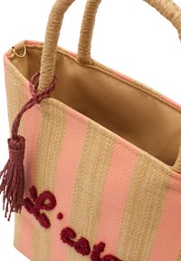 Geflochtene Strohtasche mit pink- und beige gestreiften Mustern, ausgestattet mit einem braunen gefütterten Innenraum und einem roten Quaste-Akzent an der Seite.