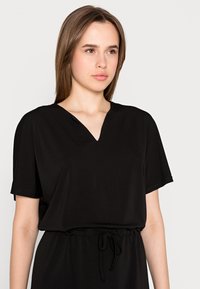 Vestido preto de decote em V com mangas curtas e cintura elástica, feito de tecido suave. Apresenta um detalhe com cordão para ajuste.