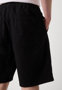 Schwarze Shorts aus strukturiertem Stoff, ausgestattet mit einem elastischen Bund und zwei Gesäßtaschen. Das Design weist ein dezentes Crinkle-Muster auf.