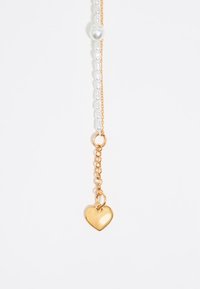 Pendente a forma di cuore dorato su una delicata catena, decorato con perline bianche, con una texture liscia e lucida. Design semplice ed elegante.