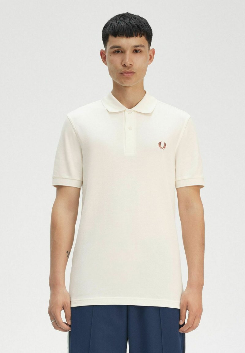 Polo bianco in tessuto strutturato, maniche corte e chiusura a tre bottoni. Presenta un piccolo logo ricamato rosso sul petto.