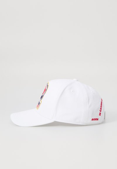 Casquette de baseball blanche avec un logo coloré brodé à l'avant et "NÉ AU CANADA" en texte rouge sur le côté. En matériau coton.