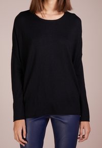Svart långärmad tröja i mjukt material med rund halsringning. Har en avslappnad passform och neddragna axelsömmar.