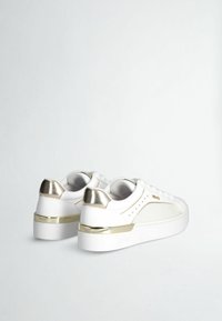 Sneakers bianchi con dettagli dorati, caratterizzati da una superficie liscia, design low-top e una suola bianca spessa con una striscia dorata sul tallone.