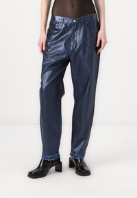Jeans metálicos de color azul oscuro de cintura alta con un corte relajado, que cuentan con bolsillos frontales y dobladillos deshilachados. Combinados con zapatos negros de tacón cuadrado.