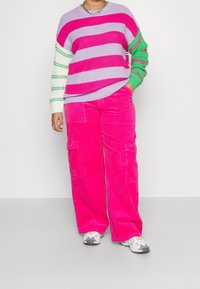 Randig tröja i lila, rosa och grön med ribbad textur, tillsammans med ljusrosa kordbyxor med fickor och lös passform.