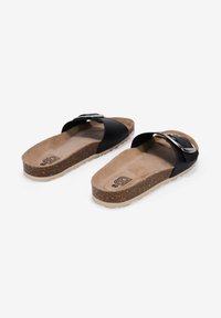 Sandalias de slide negras con una correa ancha, plantilla de corcho y suela de goma texturizada beige. Incluye un acento de hebilla plateada en la correa.