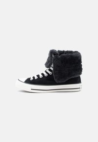 Zapatillas altas de ante negro con un cuello de peluche doblado, cordones blancos y suela de goma blanca con rayas negras.