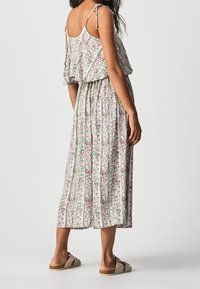 Maxi-jurk met dunne bandjes, een gerimpelde lijfje, een geplooide rok en een lichtgroene achtergrond. Geaccentueerd met roze bloemen en lichte strepen.