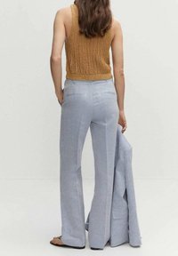 Svetle modré tailored kalhoty s rozšířeným střihem, doplněné hnědým pleteným topem bez rukávů. Modelka drží odpovídající sako.