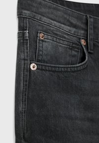 Gros plan sur la poche avant d'un jean en denim noir avec rivets métalliques et couture détaillée sur la texture du tissu.