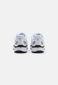Adidași albi și negri cu un superior din plasă, guler căptușit, design unic al călcâiului și talpă din cauciuc cu branding Nike.