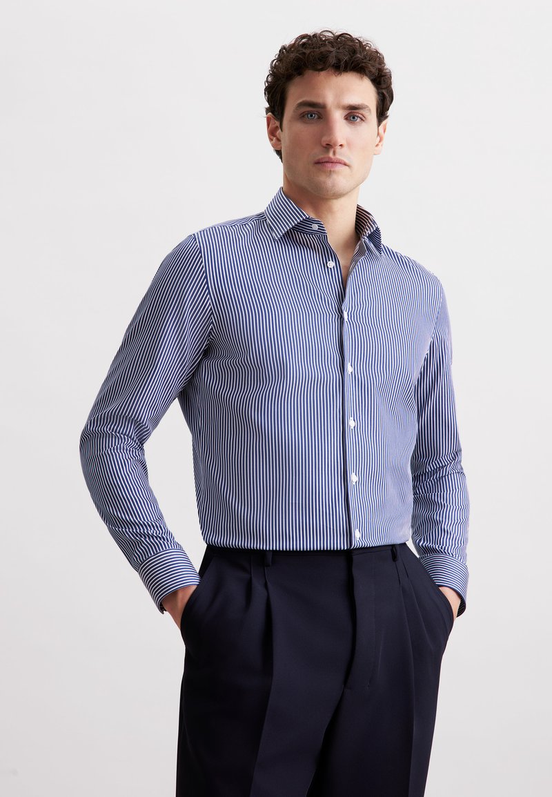 Camicia a maniche lunghe a righe blu e bianche con colletto classico. Presenta chiusura con bottoni e polsini a contrasto, realizzata in tessuto liscio.