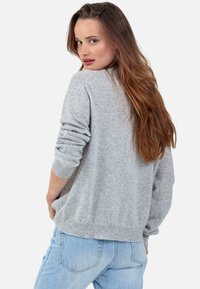 Pull gris clair en tissu doux, avec une coupe ample, des poignets et un ourlet côtelés. Associé à un jean bleu clair.