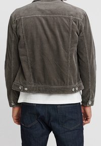 Giacca in corduroy grigio con un design aderente, chiusura a bottoni e una texture liscia. Presenta un colletto classico e un dettaglio sul giromanica posteriore.
