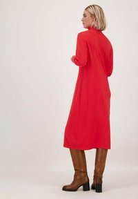 Rode lange jurk met lange mouwen en hoge hals, met een gladde textuur en een middenkuitlengte, gecombineerd met bruin kniehoog met een hak.