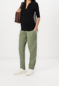 Czarna prążkowana koszulka polo, zielone spodnie w luźnym kroju, białe sneakersy i brązowa torebka z zamszu. Elementy prostego i nowoczesnego designu.