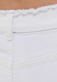 Tela de mezclilla blanca con una cintura deshilachada. Las características incluyen una textura suave, costuras visibles y un aspecto limpio y a medida.