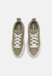 Grønne semskede sneakers med hvite snørebånd, en hvit gummisåle og en baklapp for enkel slitasje. Har merkevarelogo på innersålen.