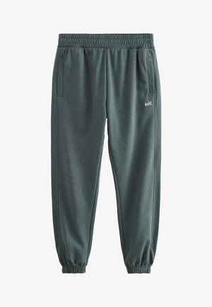 Pantaloni de trening gri închis cu talie și manșete elastice, buzunare laterale și mic logo alb „self.” pe coapsa dreaptă.