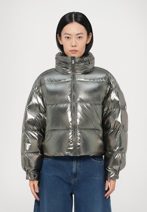 Metalen zilveren donsjack met een hoge kraag, doorgestikt ontwerp, ritssluiting aan de voorkant en elastische boorden, gecombineerd met blauwe spijkerbroek.