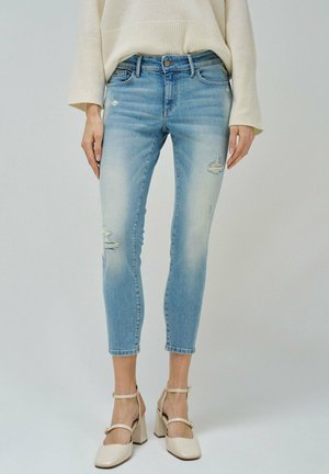 Slim-fit light blue distressed jeans worn with a cream sweater and beige high-heeled ankle strap shoes.
