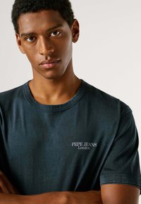 Tamnoplava kratka majica s kratkim rukavima od mekanog tkanja, s okruglim ovratnikom i suptilnim bijelim logotipom "Pepe Jeans London" na prsima.