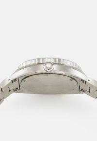 Montre en acier inoxydable avec une lunette texturée argentée, un boîtier rond et une couronne polie. Dispose d'un bracelet en maillons métalliques, mettant en avant un design simple.