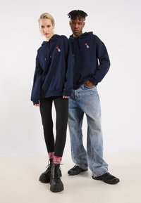 Ναυτικές φόρμες με μπροστινές τσέπες και κορδόνια, με κεντημένα σχέδια καρδιάς και ανανά. Οι μαύρες κολάν και τα τζιν με φθορές συμπληρώνουν την εμφάνιση.