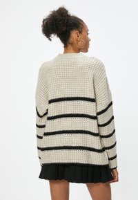 Strickpullover in Creme mit schwarzen horizontalen Streifen, runder Ausschnitt und lockere Passform. Texturiertes Material mit langen Ärmeln.