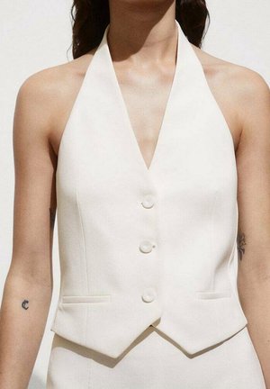 Woman wearing a sleeveless white vest with buttons and two small pockets, showing tattoos on both upper arms.