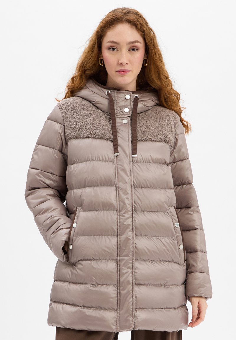 Beige gepolsterter Mantel mit Kapuze, ausgestattet mit einem braunen Fleece-Einsatz, seitlichen Taschen mit Druckknopfverschluss und einem Reißverschluss vorne. Glatte Textur in der gesamten Ausführung.