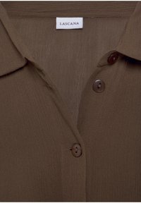 Camicia marrone con bottoni e colletto, realizzata in tessuto testurizzato. Presenta un'etichetta cucita con "LASCANA" e bottoni marroni.