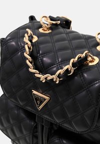 Sac à main en simili cuir matelassé noir avec une bandoulière en chaîne dorée et une plaque logo. Surface texturée avec finition brillante et accents en métal.