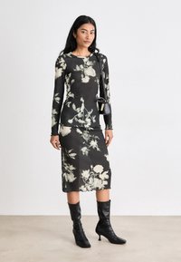 Mörkblommig klänning med långa ärmar i svart och kräm, figursydd design, midilängd, mjuk tyg; kombinerad med svarta knähöga klackstövlar och en liten handväska.