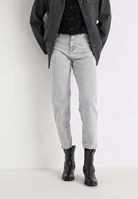 Calças de ganga cinza clarinho com um corte reto, apresentando um design clássico de cinco bolsos e bainhas dobradas. Acompanhadas de botas de tornozelo pretas.