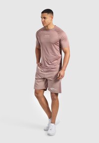 Ljusrosa sportt-shirt med korta ärmar och logotyp på bröstet, kombinerad med matchande ljusrosa shorts med sidofickor och vita detaljer.