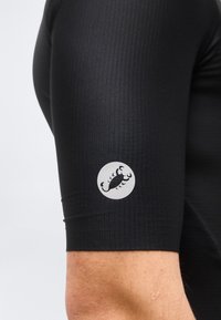 Κοντινό πλάνο του μπράτσου ενός ατόμου που φοράει μαύρο κοντομάνικο πουκάμισο με ριμπ ύφανση και αντανάκλαση λογότυπου σκορπιού στο μανίκι.